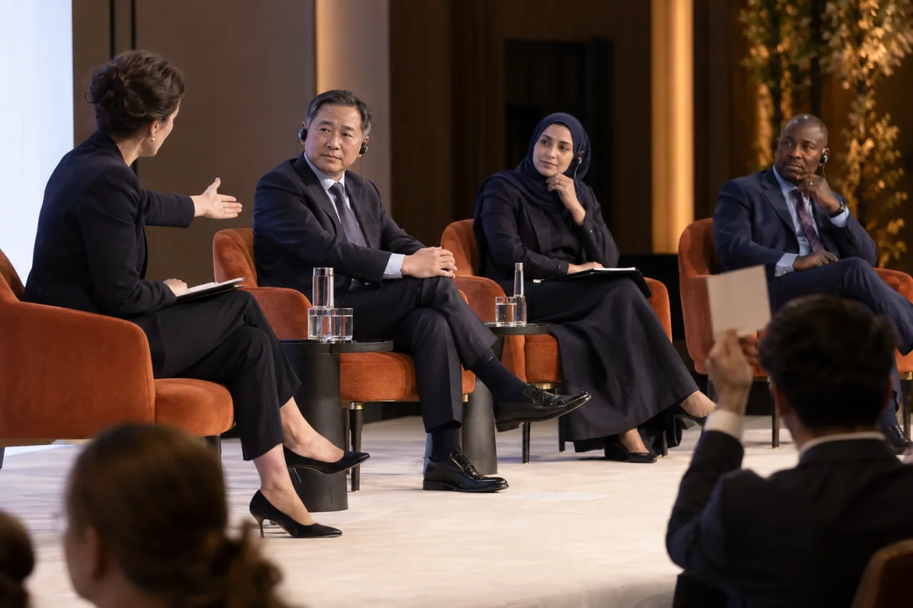 Fotografia editorial de moderadora coordenando debatedores internacionais em um painel.