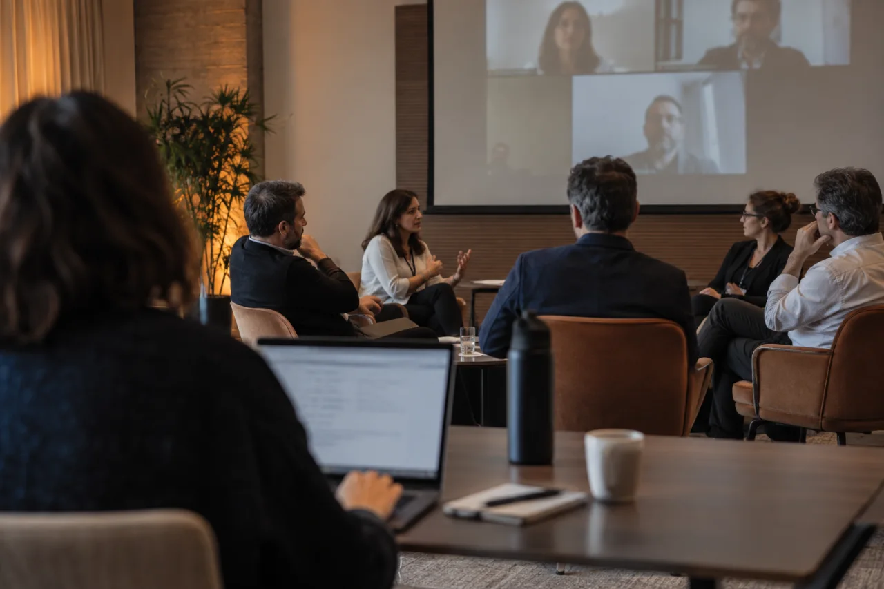 Profissional acompanha um encontro híbrido com um laptop na sala do evento.